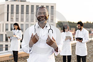 African doctor in white lab coat posing on camera with stethoscope and smiling.