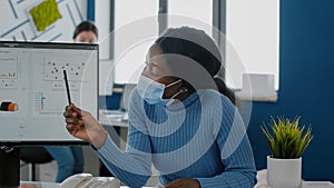 African employee with face mask explaning project to invalid coworker