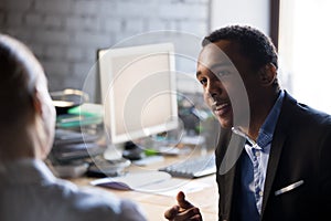 African employee talking with female colleague sitting together at workplace