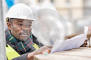 African engineer checking office blueprints on construction site