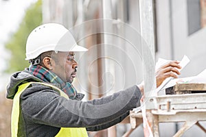 African engineer checking office blueprints on construction site