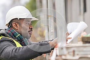 African engineer checking office blueprints on construction site