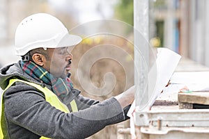 African engineer checking office blueprints on construction site