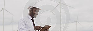 African engineer smile and using tablet with the wind turbine for inspect the operation of large wind turbines that converts wind photo