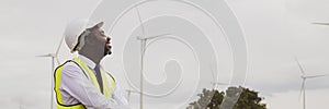 African engineer stand with smile near the wind turbine for inspect the operation of large wind turbines that converts wind energy photo