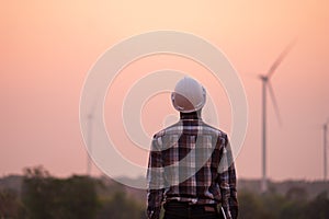 African engineer wearing white hard hat standing with digital tablet against wind turbine on sunny day