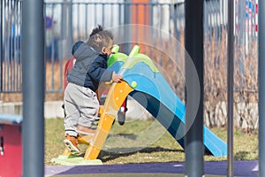 An african ethnicity 5 years old boy dreassed in winter clothing is making his way for a slide in a children's