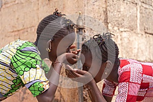 African ethnicity girls drink water from tap outside