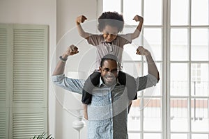 African ethnicity little son sitting on fathers shoulders showing biceps