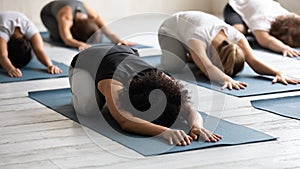 African ethnicity woman and associates lying on mats practicing Balasana