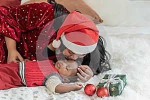 Nigerian mother wearing a red Christmas hat and kissing head her 4-month-old baby newborn son lying and sleeping in bed with happy