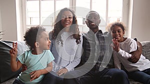 African family sitting on couch waving hands looking at camera