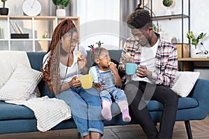 African family of three enjoying snack break on comfy couch
