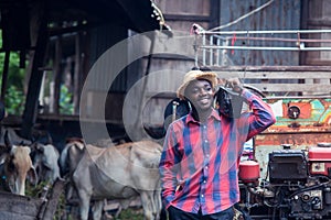 African farmer man with retro radio broadcast receiver on shoulder stands happy smiling outdoor on old cow stall background