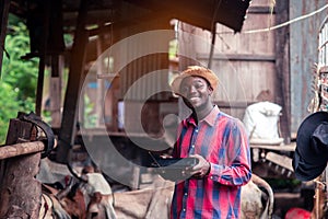 African farmer man with retro radio broadcast receiver on shoulder stands happy smiling outdoor on old cow stall background