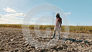 African farmer walking acros the plowed agricultural field with corn and powerline in the background.