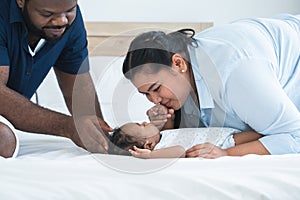 African father and Asian mother kissing hand of cute newborn baby sleeping lying on bed, smiling looking at innocent infant with