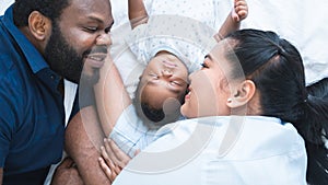 African father and Asian mother lying with cute newborn baby sleeping on bed at home, parents smiling looking at infant with love
