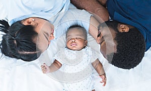 African father and Asian mother lying with cute newborn baby sleeping on bed at home, parents smiling looking at infant with love