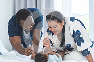 African father and Asian mother playing talking with cute newborn baby lying on bed, smiling looking at innocent infant with love