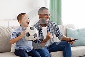 African Father And Son Watching Sports On TV At Home