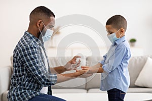 African Father Spraying Sanitizer On Son's Hands At Home