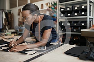 African female artisan using a pattern on leather in her shop