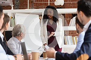 African female business coach talk to employees give flipchart presentation