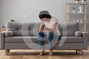 African female crying feels unhappy sitting on couch at home