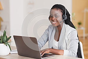 African female customer support operator wearing headset and working on laptop