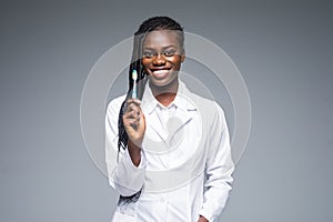 Beautiful african female dentist doctor holding and showing a toothbrush isolated on a gray background