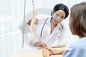 African female doctor consulting with European patient about her back with plastic bone structure anatomical in hospital