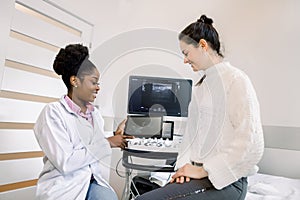 African female doctor gynecologist or obstetrician showing ultrasound photo of baby to young pregnant woman. Ultrasound