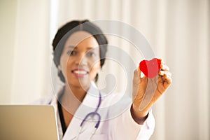 African female doctor with stethoscope stand and holding a red heart symbol.