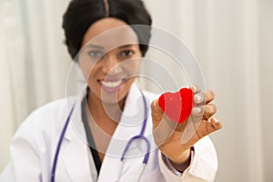 African female doctor with stethoscope stand and holding a red heart symbol.