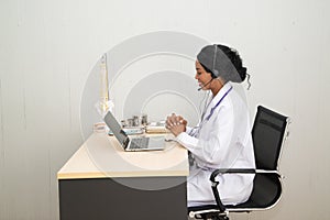 African female Doctor looking on laptop computer while sitting at the desk in hospital office.