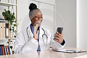 African female doctor video calling patient in online mobile phone app.