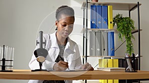 African female scientist doing some research and looking through a microscope in laboratory
