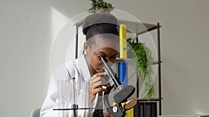 African female scientist doing some research and looking through a microscope in laboratory