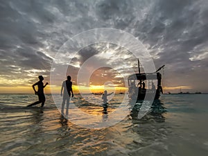 African fishermen on a wooden boat swim up to the shore. Sunset