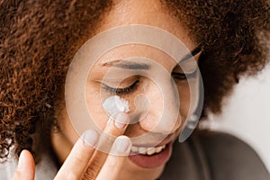 African girl applying face moisturizer cream close-up to protect skin from dryness in bath. African american woman in