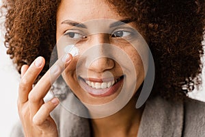 African girl applying face moisturizer cream close-up to protect skin from dryness in bath. African american woman in