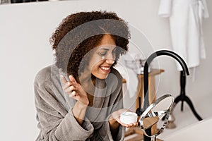 African girl applying face moisturizer cream to protect skin from dryness in the bath. African american woman in