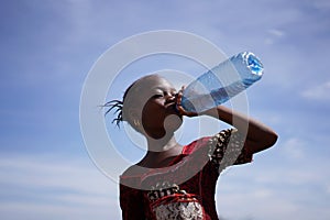 African Girl Drinking From a Water Bottle Under An Intensely Blue Sky