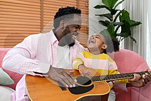 African girl and father are playing guitar while sitting on the sofa at home