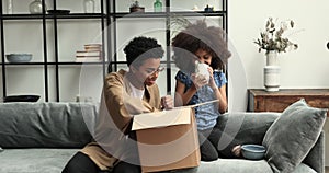 African girl her mother unpack parcel box with diverse kitchenware