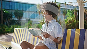 African girl reading book sitting on street bench close up. Student studying