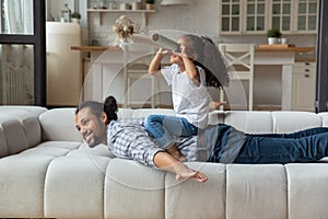 African girl sit on daddy back looks into paper tubes