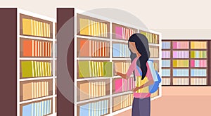 African girl student choosing books schoolgirl near bookshelves modern library interior reading education knowledge