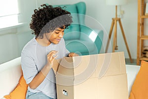 African girl unpacking delivery looking in box. Happy woman opening carton box. Female getting parcel looking at